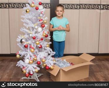 Seven-year girl stands in a box with Christmas toys and Christmas tree. Seven-year girl shoots with a Christmas tree ornaments