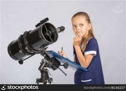 Seven-year girl thoughtful looking at the sky, making the recording of observations in the telescope