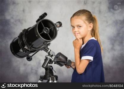 Seven-year girl thoughtfully looks in the picture, standing at the telescope