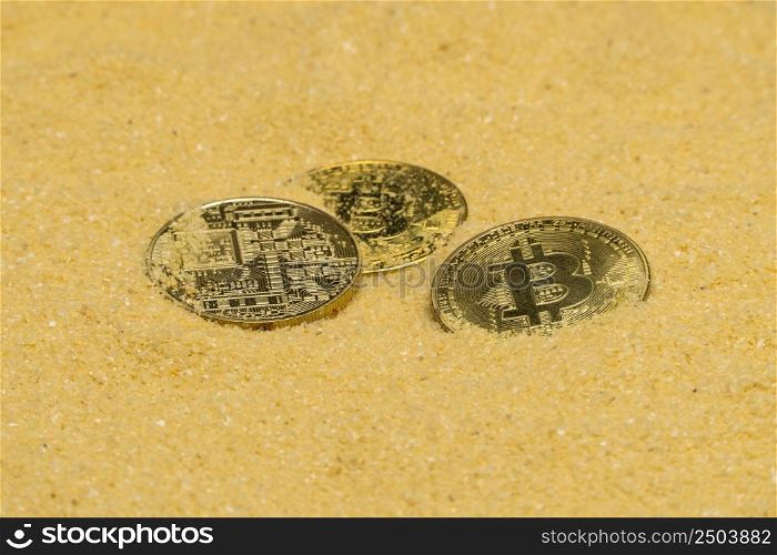several bitcoin crypto coins on brilliant golden sand. finding and mining cryptocurrency. bitcoin on golden sand