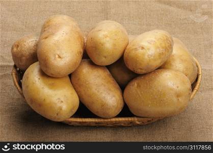 Several brown potatoes in a basket on a sacking