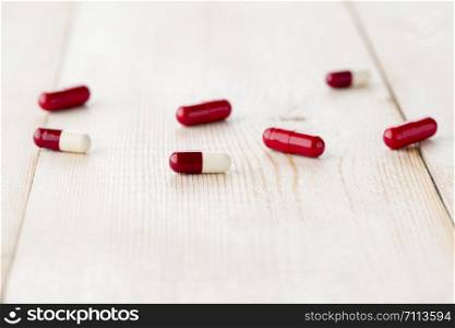 several different soluble red and white drug capsules for ingestion. A close-up on a bright wooden table. Different red and white drug capsules for ingestion. A close-up on a bright wooden table