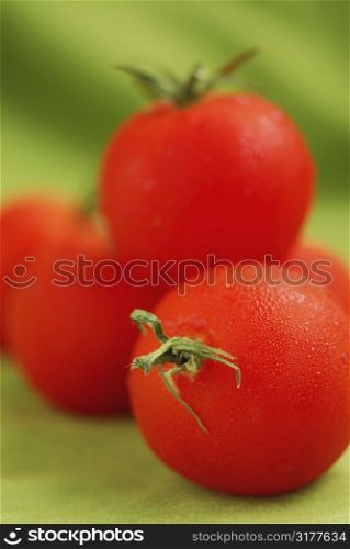 Several fresh dewy tomatoes close up on green background
