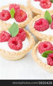 Several fruit tartlets with red raspberries on a wooden surface closeup