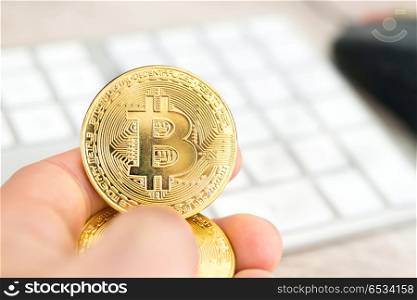 Several golden bitcoins in a hand near white keyboard and computer mouse. Electronic money mining concept. Several golden bitcoins in a hand