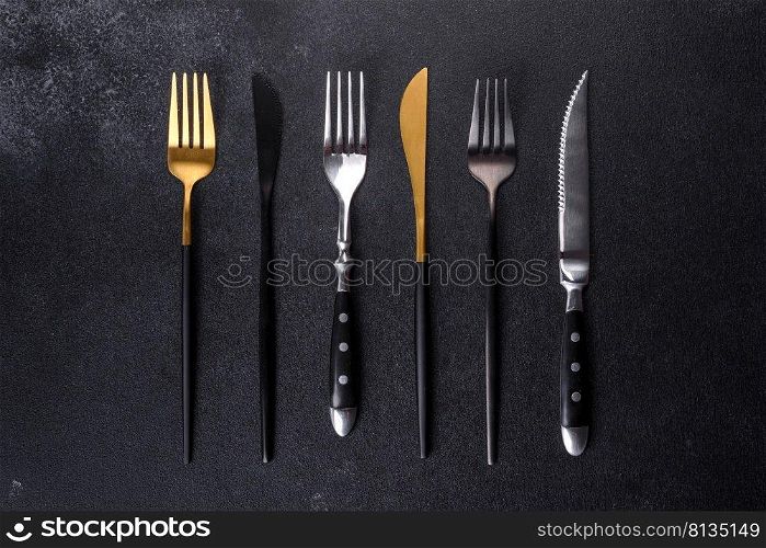 Several knives and forks in black gold and silver on a dark concrete background. Preparing the table for lunch. Several knives and forks in black gold and silver on a dark concrete background