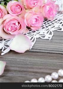 Several pink roses, pearl necklace and knitted lace doily on the old gray boards