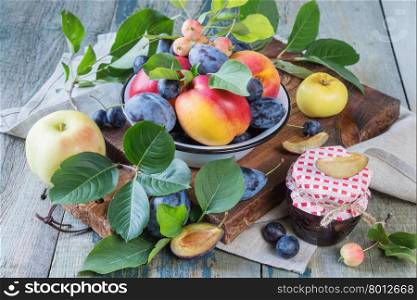 Several red nectarines with green leaves, blue plums and prunes in a enamelled bowl on the old wooden table