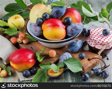 Several red nectarines with green leaves, blue plums and prunes in a enamelled bowl on the old wooden table