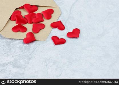 Several red silk hearts flying out of an open postal envelope made of kraft paper on a gray stone background, with copy-space