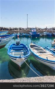 Several small colorful boats are anchored in the harbor of Catania, SIcily-Italy on the coast of the Mediterranean Sea.
