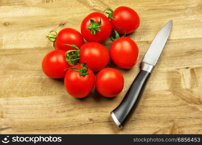 Several small red tomatoes and a knife lie on a wooden surface