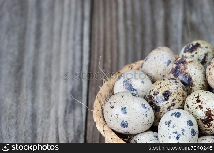 Several spotted quail eggs in a wicker basket on the background of the old wooden boards