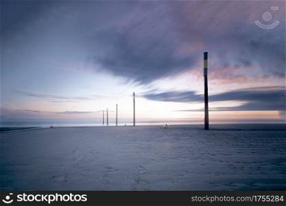 Several tall wooden poles with yellow stripe for marking coastline. Sunset sky with colorful clouds. Long exposure.