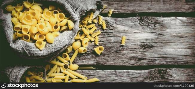 Several types of pasta in old bags. On wooden background. Free space for text . Top view. Several types of pasta in old bags.