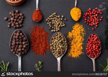 Several types of spices in metal spoons paprika, tomatoes, curry, beets, cumin, turmeric, fennel, spirulina, allspice of different colors on a black concrete background
