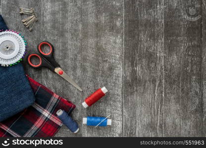 Sewing accessories, denim and plaid fabric on a dark wooden background. Fabric, sewing threads, needle, pins and scissors. Copyspace. Sewing accessories, Jeans and plaid fabric on a dark wooden background. Fabric, sewing threads, needle, pins and scissors. top view, flatlay