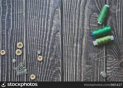 Sewing accessories on dark wooden background. Green sewing threads, needles, buttons and pins. top view, flatlay. Copyspace. Sewing accessories on dark wooden background. Green sewing threads, needles, buttons and pins. top view, flatlay