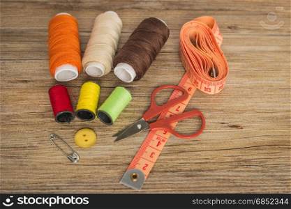 Sewing background. Accessories for needlework on wooden background. Spools of thread, scissors, buttons, measuring tape, sewing supplies. Set for needlework top view with copy space.