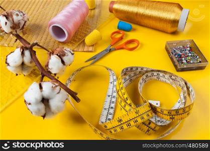 sewing items on a yellow background with a branch of wild cotton