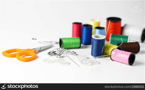Sewing kit for tailoring with colorful cotton threads of different sizes, needle, scissor and buttons close up view on white background.
