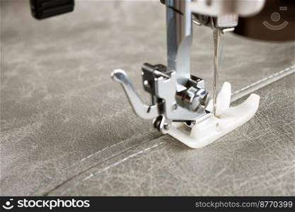 sewing machine with special presser foot makes a seam on grey leather. sewing process close up. sewing machine presser foot and item of clothing