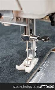 sewing machine with special presser foot makes a seam on grey leather. sewing process close up. sewing machine presser foot and item of clothing