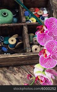 Sewing supplies and Orchid. Wooden box with thread and buttons for crafts and blooming Orchid