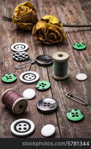 sewing thread, with buttons on wooden background with buds dried yellow roses