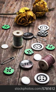 sewing thread, with buttons on wooden background with buds dried yellow roses