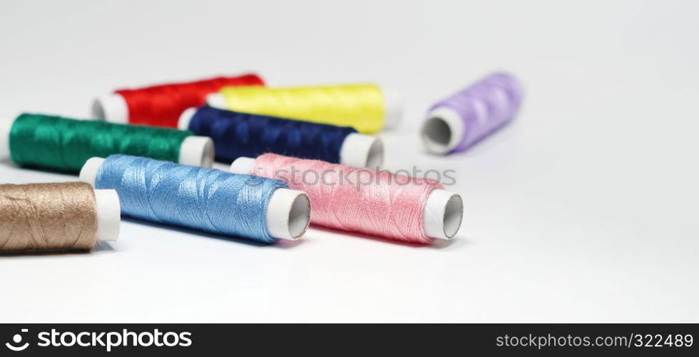 Sewing threads in different colors close up on white background with copy space.