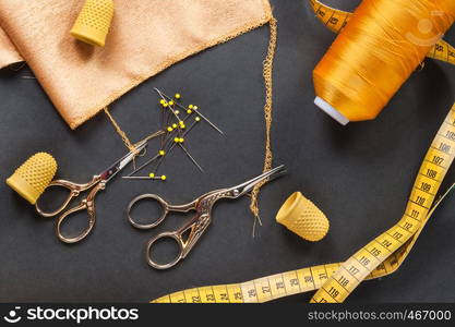 sewing tools thread with scissors and measuring tape on dark