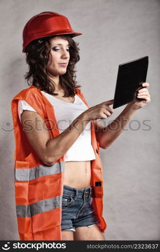 Sex equality and feminism. Sexy girl in workwear safety helmet and orange vest using tablet touchpad. Attractive woman as construction worker. Technology.