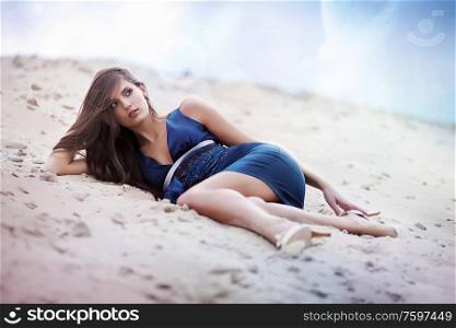 Sexual brunette woman in blue dress laying on the cosmic beach