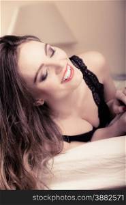 Sexuality and temtation of women. Attractive seductive long curly hair woman in black lingerie on bed. Indoor.
