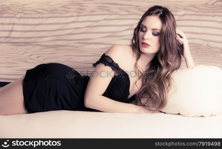 Sexuality and temtation of women. Attractive seductive long curly hair woman in black lingerie on bed. Indoor.