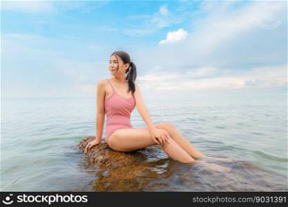 Sexy asian woman Wear a pink body suit. Sitting on a rock in the sea