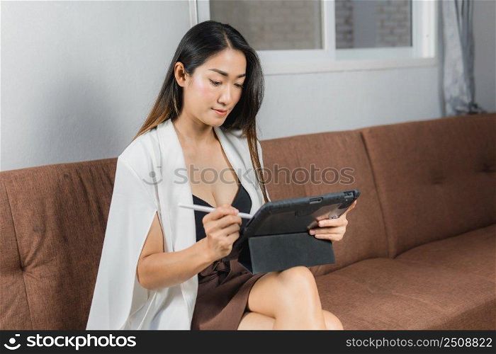 Sexy asian women sitting on the sofa working with a tablet, concept work from home.