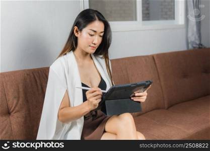 Sexy asian women sitting on the sofa working with a tablet, concept work from home.