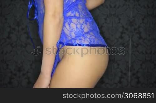 Sexy bare buttocks of a woman in blue lingerie standing sideways to the camera against a dark background in a provocative pose