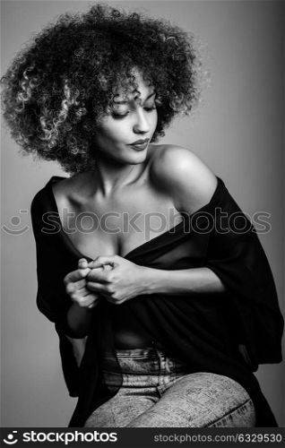 Sexy black woman with afro hairstyle. Girl wearing black shirt and blue jeans. Studio shot. Black and white photograph.