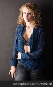sexy blond curly haired woman in blue shirt and bra on black background