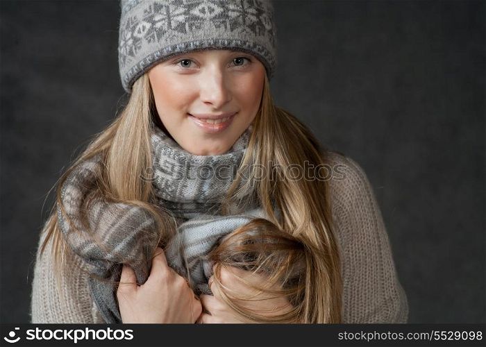 Sexy blond haired female smiling and looking at camera. Portrait of woman on dark background wearing woolen accessories