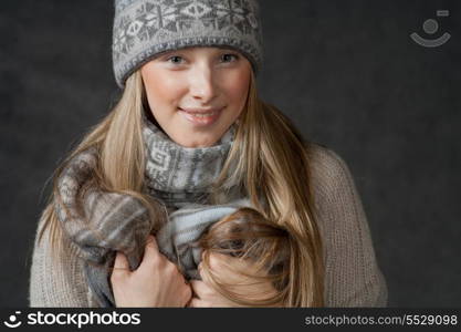 Sexy blond haired female smiling and looking at camera. Portrait of woman on dark background wearing woolen accessories