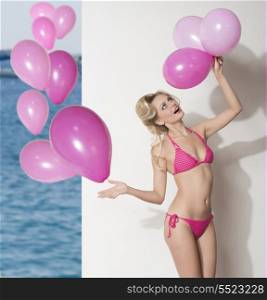 sexy blonde female wearing pink swimwear and playing with balloons. Funny portrait , summertime.