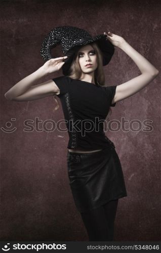 sexy blonde girl with long cute hair and dark make-up posing with gothic clothes and witch hat in Halloween portrait