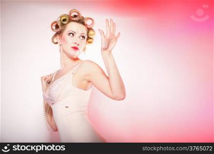 Sexy blonde woman preparing to party, girl in underwear with curlers in hair looking on nails pink background