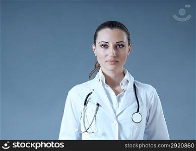 Sexy brunette doctor ready to serve you. Multiuse grey background studio portrait. Wearing white-coat with open discreet face and stethoscope on shoulders. Healthcare collection.