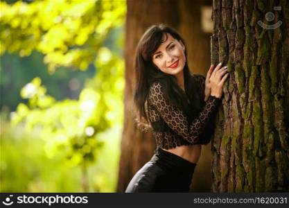 sexy brunette girl in a lace blouse and leather skirt with high heels posing near a tree in the woods.. sexy brunette girl in a lace blouse and leather skirt with high heels posing near a tree in the woods