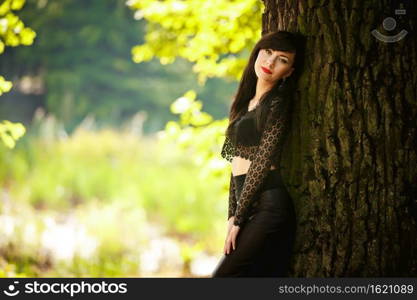 sexy brunette girl in a lace blouse and leather skirt with high heels posing near a tree in the woods.. sexy brunette girl in a lace blouse and leather skirt with high heels posing near a tree in the woods